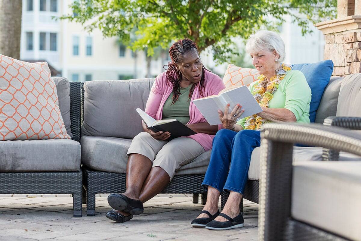 A Woman Reading A Book While Another Woman Sits On A Couch